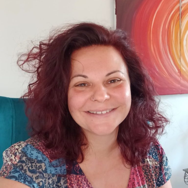 DI Barbara Lipp, MA (achtsamer Ordnungscoach) Person mit lockigem, dunklem Haar und lächelndem Gesicht, trägt große Ohrringe und ein blaues Oberteil.