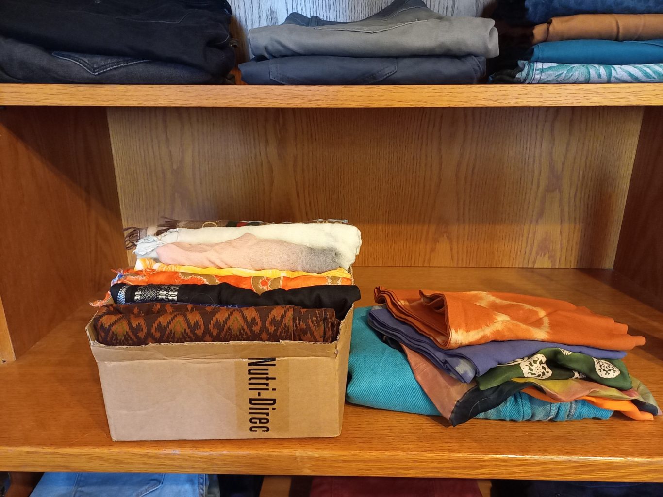Organisation von Tüchern Bunt gefaltete Stoffe und ein Karton auf einem Holzregal.