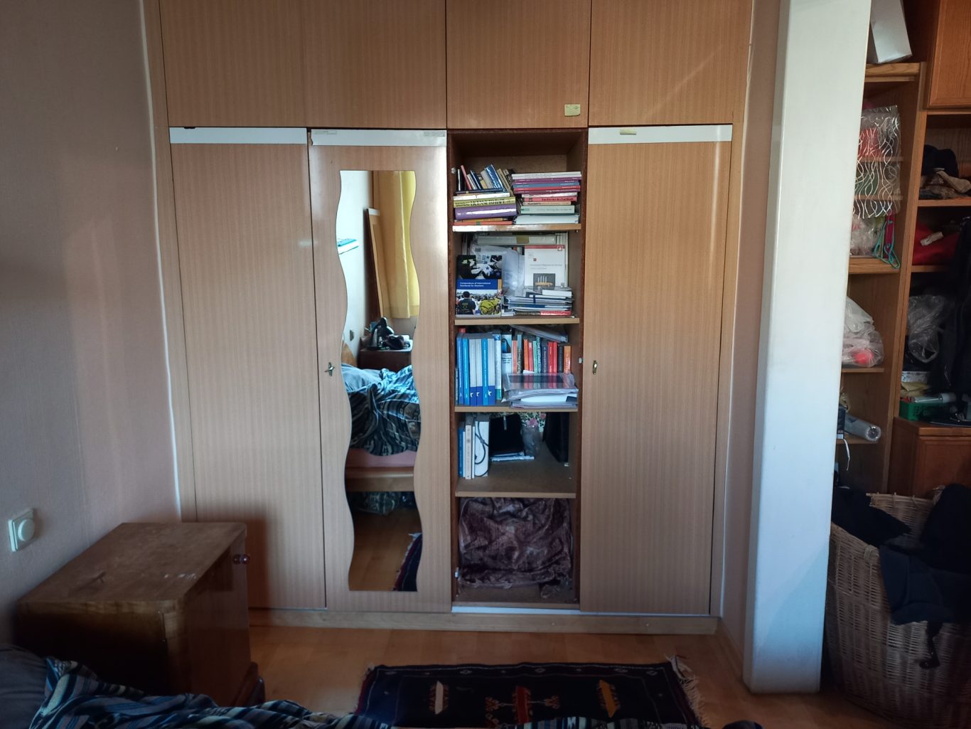 Nachher rechte Seite - Detailbild Ein Holzkleiderschrank mit Spiegel und offenen Regalen, voll mit Büchern und Gegenständen.