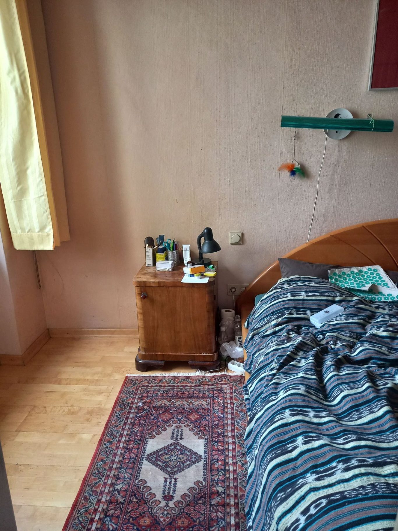 Schlafbereich nachher Ein Schlafzimmer mit Bett, Nachttisch und einem bunten Teppich. Tageslicht fällt durch das Fenster.