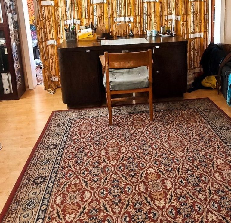 Schreibtisch nachher Ein Raum mit einem Stuhl, einem Schreibtisch und einem dekorativen Teppich. Gardinen im Hintergrund.
