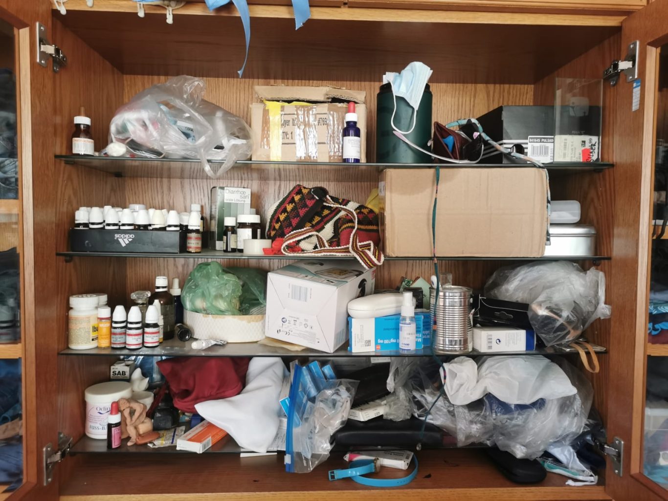 Vorher Medizinschrank Ein unordentlicher Regalschrank mit verschiedenen Medikamenten, Verpackungen und Utensilien.